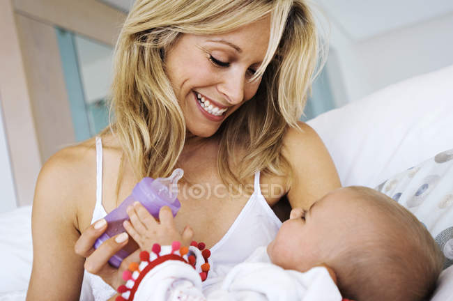 Retrato de una madre rubia sonriente alimentando al bebé en casa - foto de stock