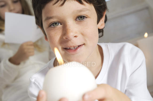 Портрет маленького хлопчика, який тримає свічку з сестрою на фоні — стокове фото