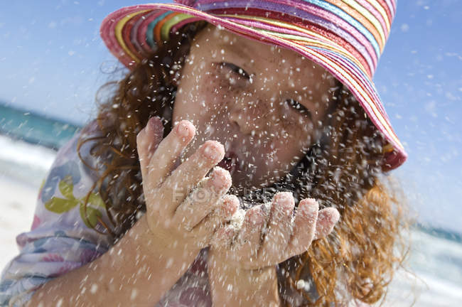 Portrait of little girl blowing sand in hands on beach — Stock Photo