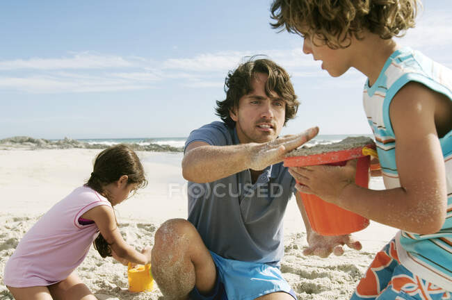 Père et deux enfants jouent sur la plage, à l'extérieur — Photo de stock