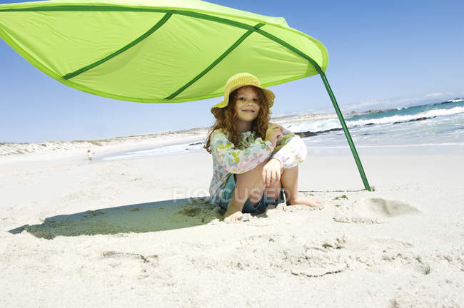 Petite fille assise sur la plage tente verte et regardant la caméra — Photo de stock