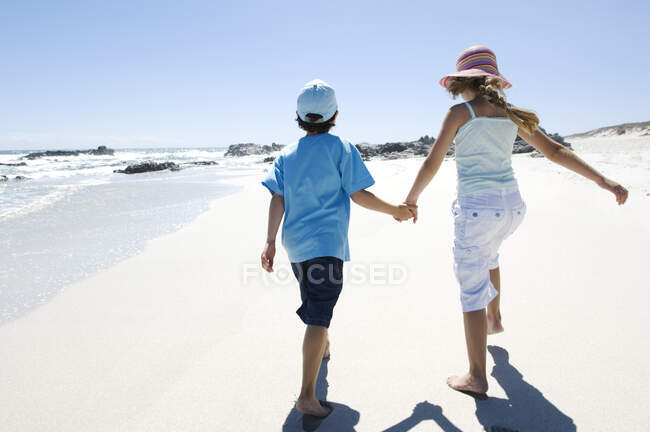 Брат и сестра гуляют по пляжу, вид сзади, на открытом воздухе — стоковое фото