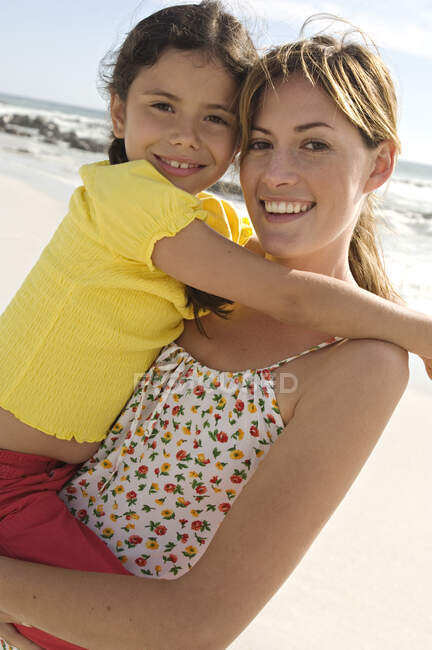 Retrato de uma mãe carregando sua filha, sorrindo, posando para a câmera, ao ar livre — Fotografia de Stock