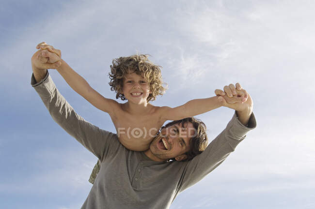 Retrato de un padre llevando a su hijo en la espalda, al aire libre - foto de stock