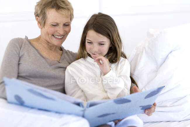 Mujer mayor y niña en la cama, mirando álbum de fotografía - foto de stock