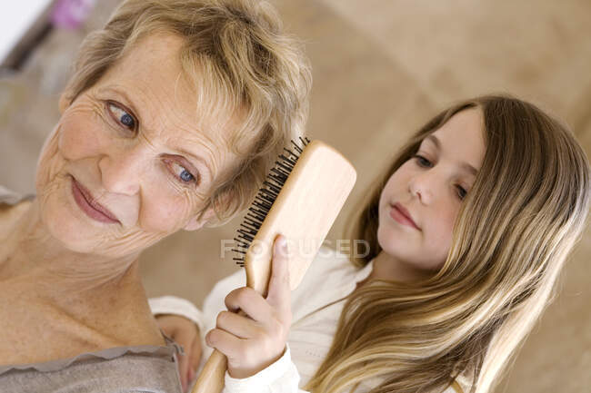 Petite fille brossant les cheveux de la femme âgée, à l'intérieur — Photo de stock