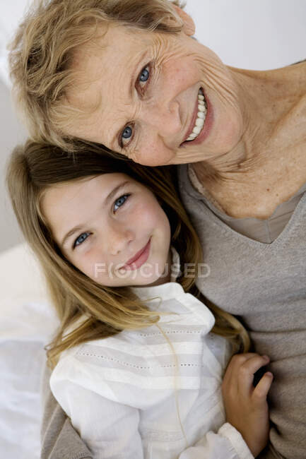 Mulher sênior e menina sorrindo para a câmera, dentro de casa — Fotografia de Stock