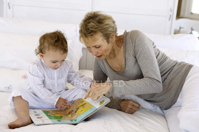 Donna anziana che legge con bambina, sul letto — Foto stock