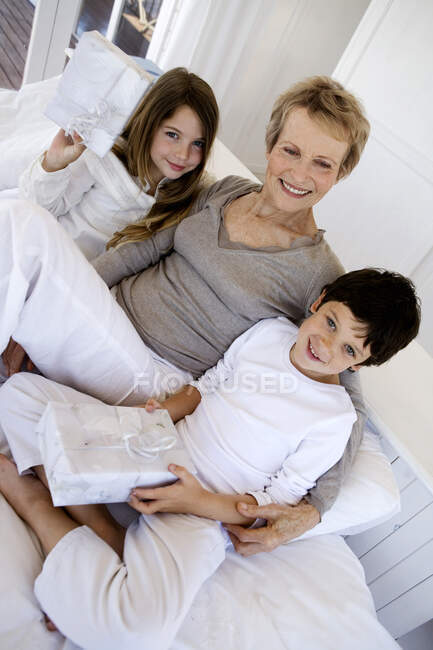 Mulher sênior e duas crianças segurando presentes, dentro de casa — Fotografia de Stock