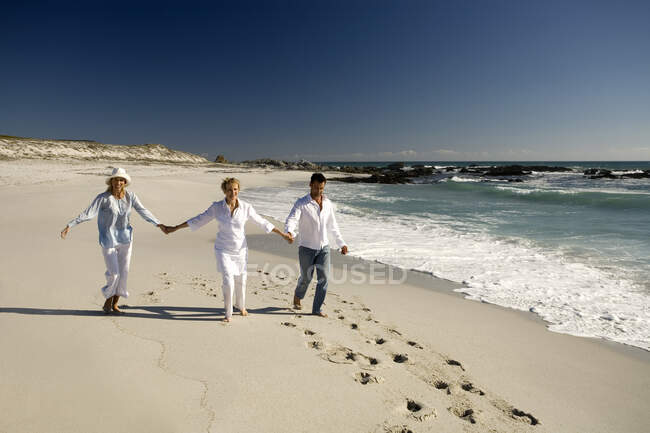 Пара и пожилая женщина держатся за руки на пляже — стоковое фото
