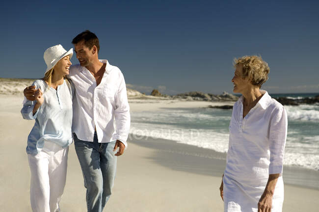 Couple embracing and senior woman waking on the beach — Stock Photo