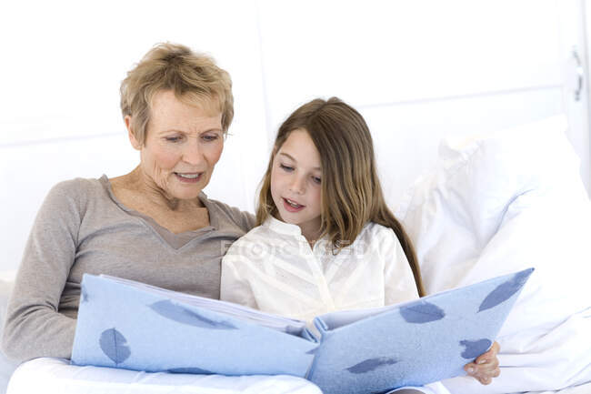 Senior woman and little girl in bed, looking at photograph album — Stock Photo