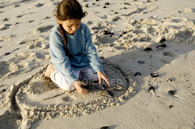 Kleines Mädchen spielt mit Muscheln am Sandstrand — Stockfoto