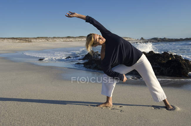 Junge blonde Frau dehnt sich sandig am Strand — Stockfoto