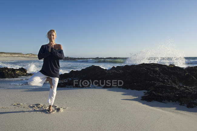 Smiling young woman in yoga attitude on beach — Stock Photo