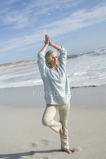 Зрелая женщина, занимающаяся йогой на песчаном пляже — стоковое фото