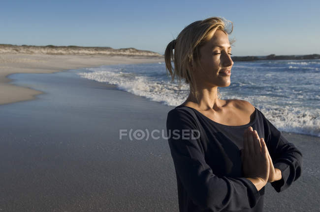 Relaxed young woman in yoga attitude on beach — Stock Photo