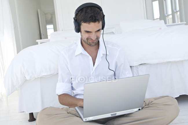 Junger lächelnder Mann benutzt Laptop auf dem Fußboden im Schlafzimmer — Stockfoto