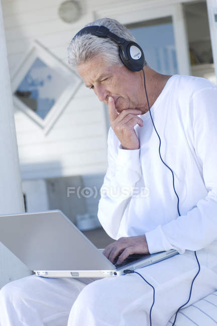Hombre mayor con auriculares utilizando el ordenador portátil - foto de stock