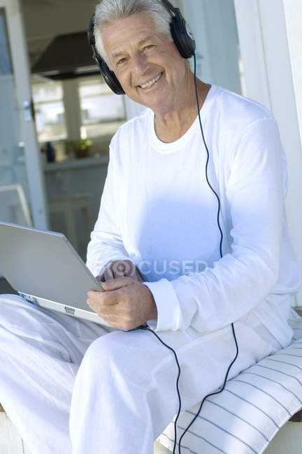 Sorrindo homem com fones de ouvido usando laptop e olhando para a câmera — Fotografia de Stock