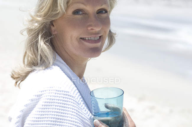 Ritratto di donna sorridente sulla spiaggia che tiene un bicchiere d'acqua — Foto stock