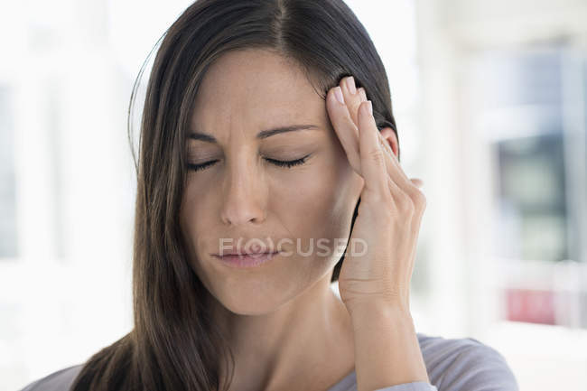 Primer plano de la mujer que sufre de dolor de cabeza sobre un fondo borroso - foto de stock