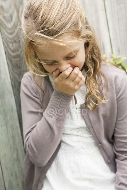 Close-up of cute little girl laughing against wooden fence — Stock Photo
