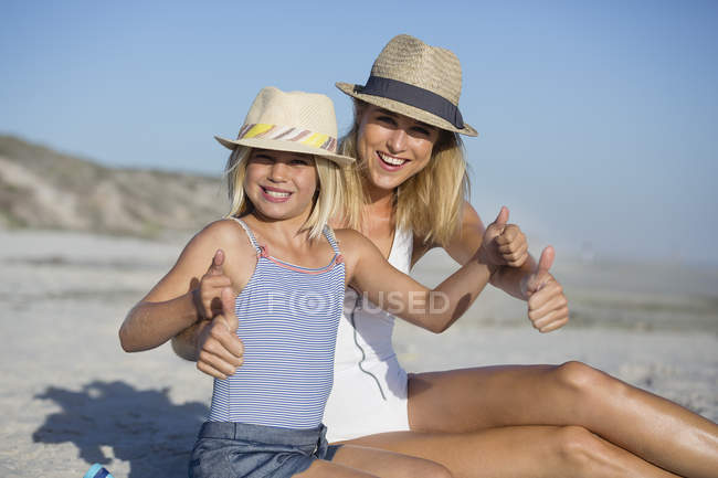 Portrait de mère et fille heureuses en chapeaux gesticulant sur la plage — Photo de stock