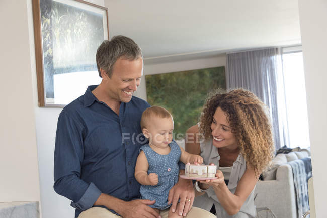 Счастливая женщина дарит игрушку маленькой дочери, сидящей на коленях отца — стоковое фото