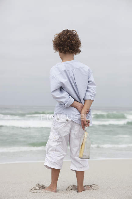 Boy holding bottle with message on sandy beach — Stock Photo