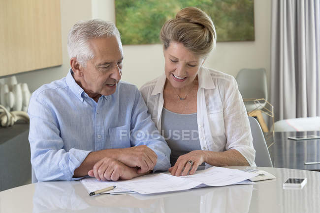 Старшая пара делает бумажную работу за столом дома — стоковое фото