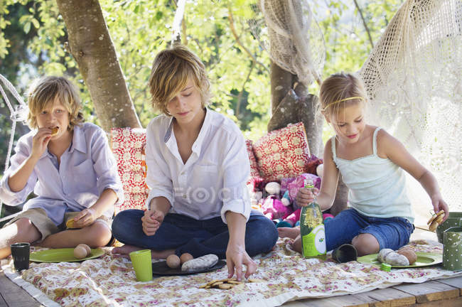 Діти їдять їжу в будинку на дереві в літньому саду — стокове фото