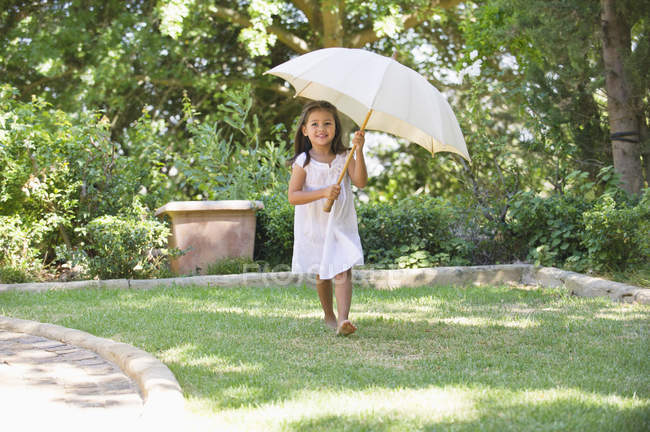 Menina bonito no vestido de verão branco segurando guarda-chuva no jardim ensolarado — Fotografia de Stock