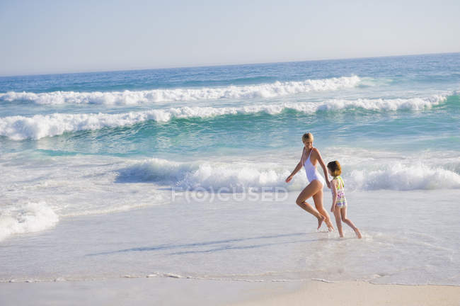 Mulher correndo na praia de areia com a filha — Fotografia de Stock
