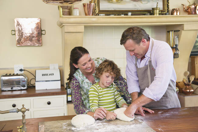 Menino bonito e seus pais amassar massa na cozinha — Fotografia de Stock