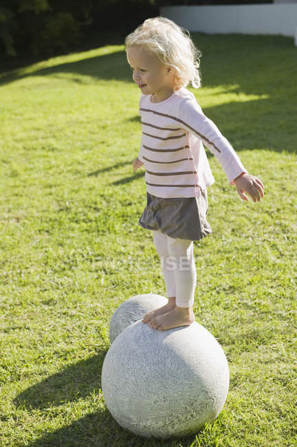 Girl balancing on stone sphere on green lawn — Stock Photo