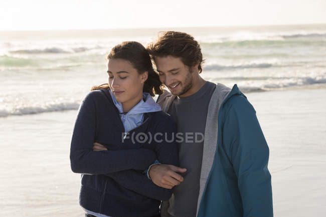 Feliz pareja joven y romántica caminando en la playa en otoño - foto de stock