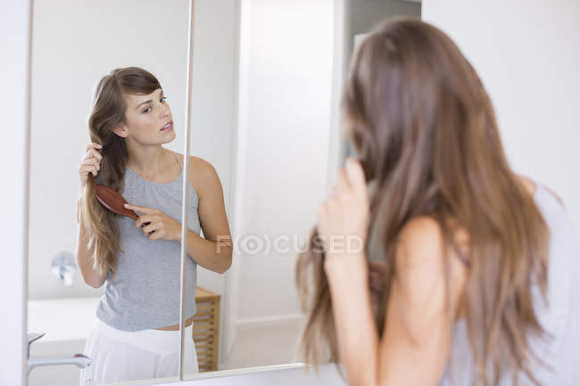 Woman combing hair in front of mirror in bathroom — Stock Photo