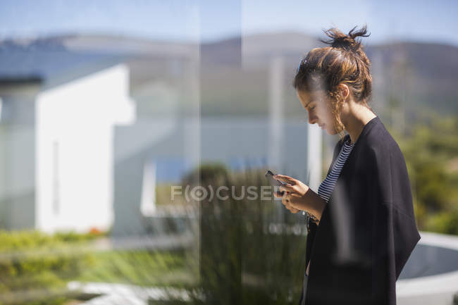 Задумчивая молодая женщина, используя смартфон, стоя на улице — стоковое фото