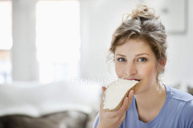 Retrato de una mujer sonriente comiendo tostadas con crema untada - foto de stock