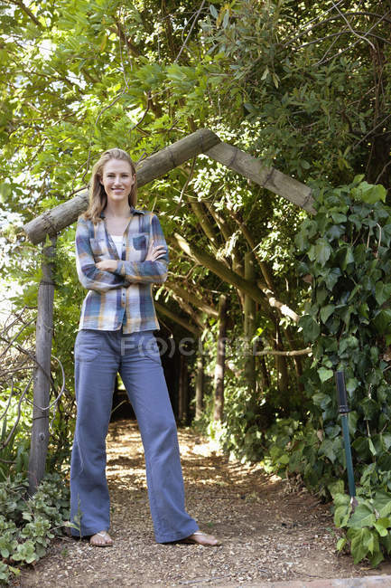 Portrait of young woman standing in garden with arms crossed — Stock Photo