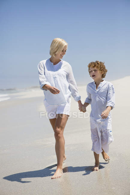 Mujer caminando en la playa con su hijo - foto de stock