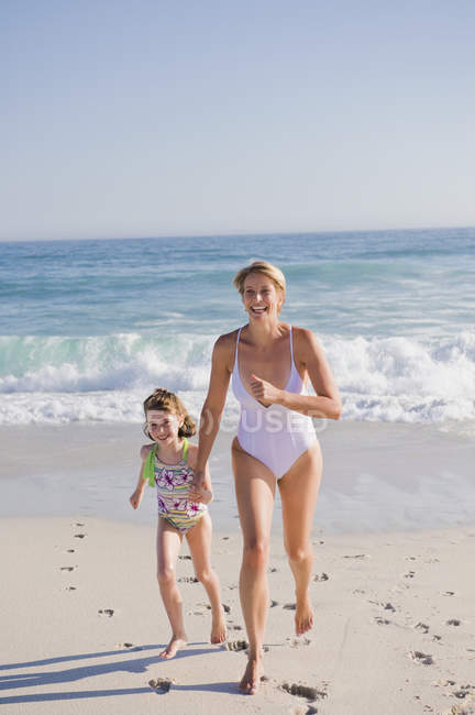 Woman running on sandy beach with daughter — Stock Photo