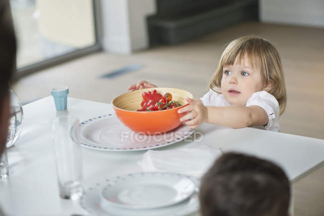 Petite fille plaçant bol sur table à manger — Photo de stock