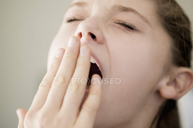 Крупный план девочки-подростка зевающей с рукой на лице — стоковое фото