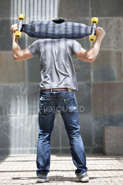 Rückansicht eines lächelnden jungen Mannes mit Skateboard auf den Schultern — Stockfoto