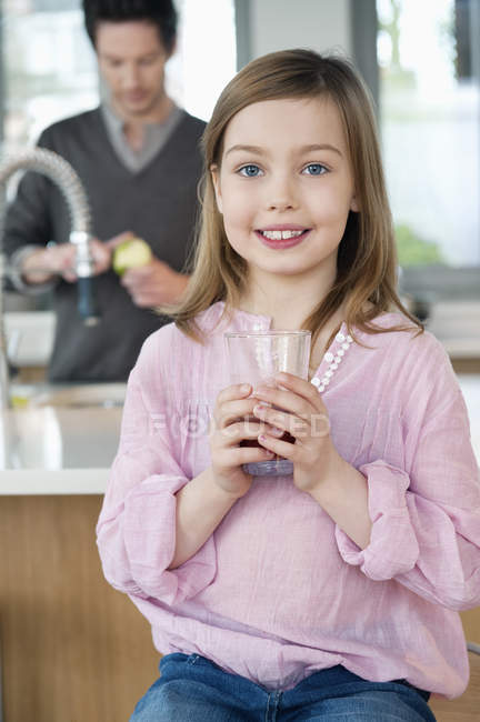 Menina beber suco com o pai de pé no fundo na cozinha — Fotografia de Stock