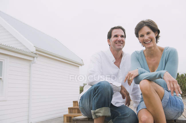Happy laughing couple sitting together in front of house — Stock Photo