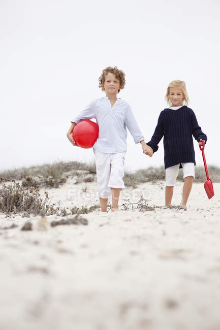Geschwister halten sich an Händen und gehen am Sandstrand spazieren — Stockfoto