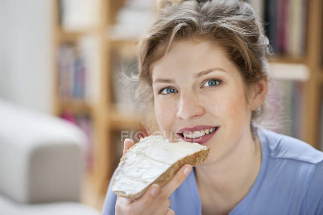 Retrato de una mujer sonriente comiendo tostadas con crema untada - foto de stock